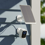 Produktfoto einer Überwachungskamera mit angeschlossenem Solarpanel darüber. Beide Komponenten sind an die Holzfassade eines Gebäudes montiert.