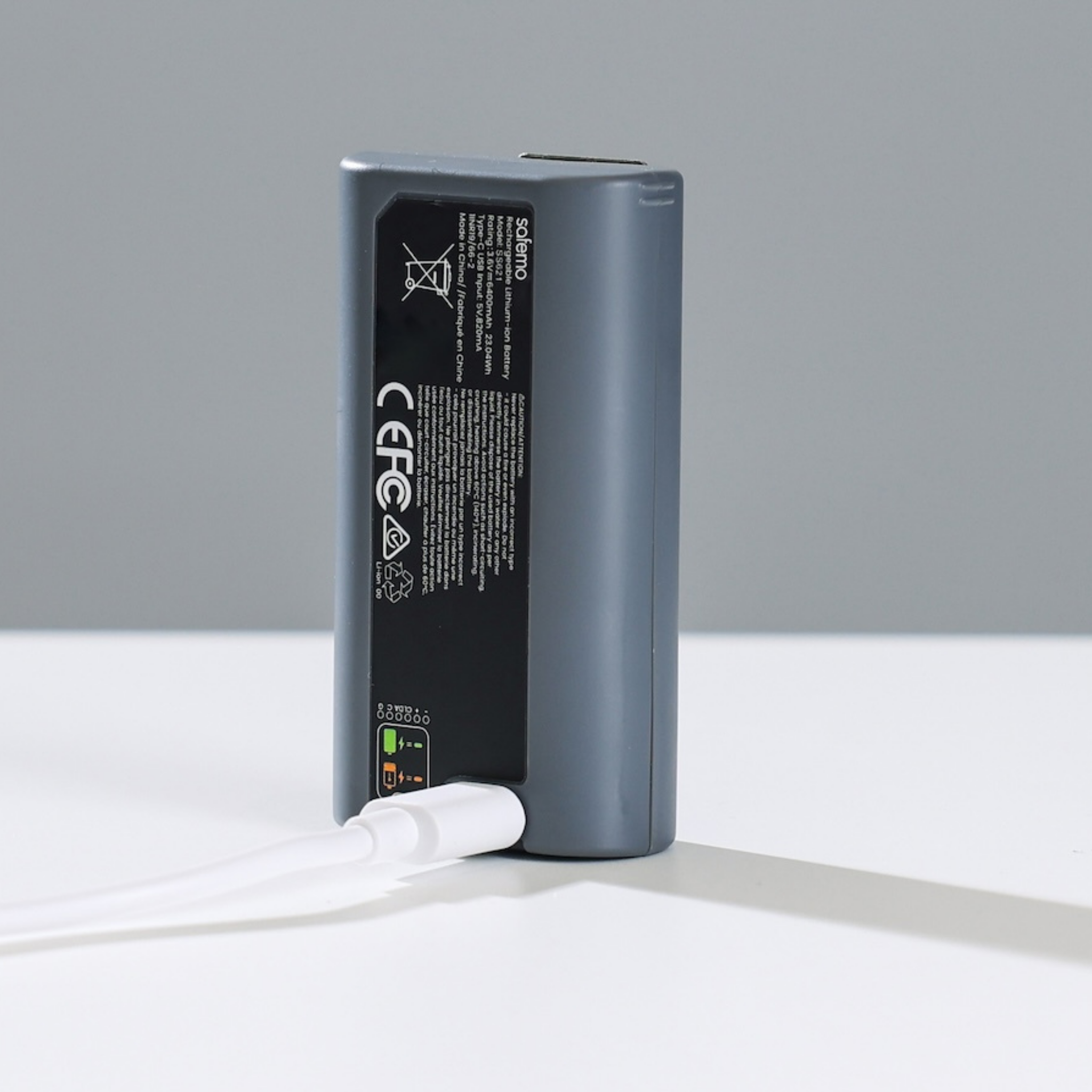 Produktfoto von Ersatzakku für Überwachungskamera verbunden mit weißem Aufladekabel.